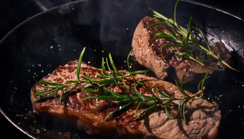 Deux steaks de vache Black Angus savoureux mijotent dans une poêle, ornés de romarin frais et de gros sel.