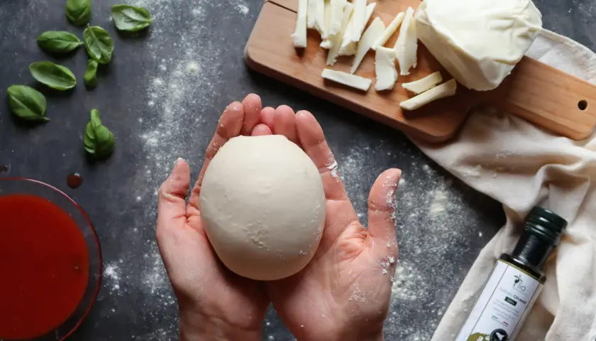 Hände halten Teigkugel für Caputo Nuvola Rezept. Mozzarella, Basilikum und Tomatensauce liegen bereit.