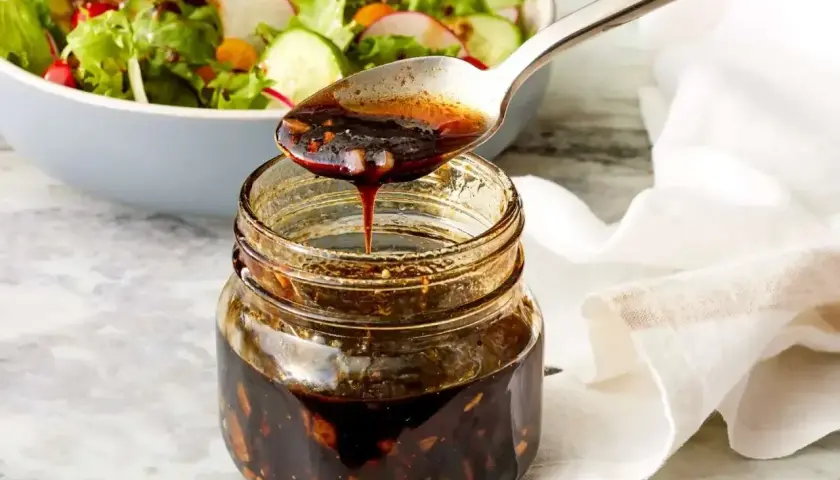 Łyżka polewa sałatkę gęstym, ciemnym sosem balsamicznym z słoiczka.
