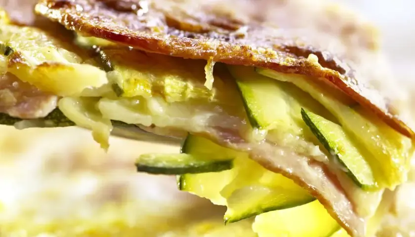 Una fetta di parmigiana di zucchine bianca, con strati di zucchine, formaggio filante e una crosticina dorata.