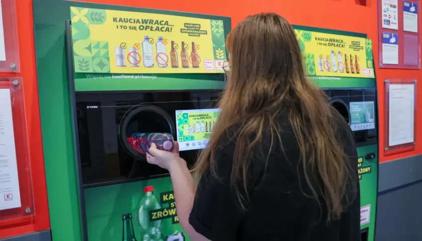 Kobieta wrzuca plastikową butelkę do automatu, który obsługuje system kaucyjny. To ekologiczne rozwiązanie, które zwraca pieniądze.