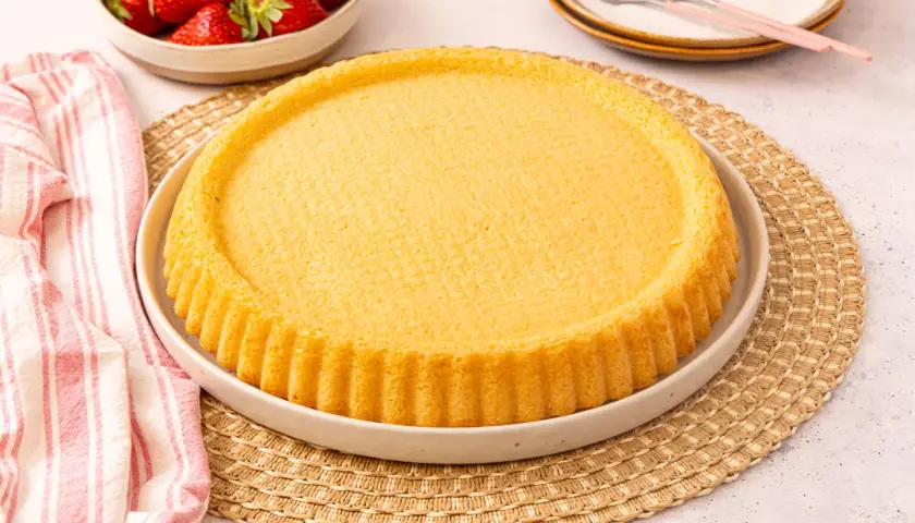 Ein goldbrauner, runder Kuchenboden, perfekt für ein Erdbeerboden Rezept. Daneben eine Schüssel mit frischen Erdbeeren.