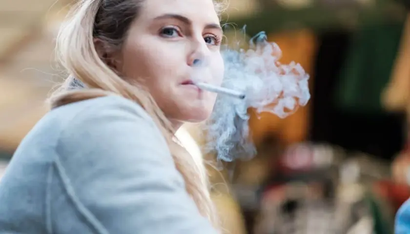 Ragazza bionda con sigaretta tra le labbra, fumo denso che le avvolge il viso. Un momento di pausa, forse dopo essersi lavata i denti, per fumare.