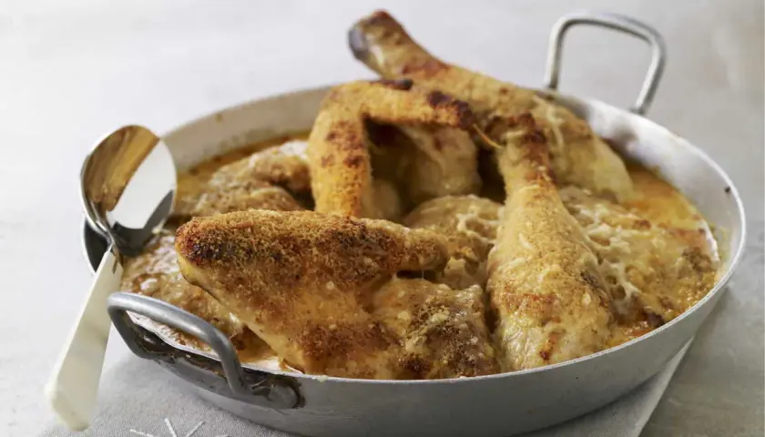Un plat de poulet Gaston Gérard gratiné, doré et croustillant, servi dans un plat en métal avec une cuillère.