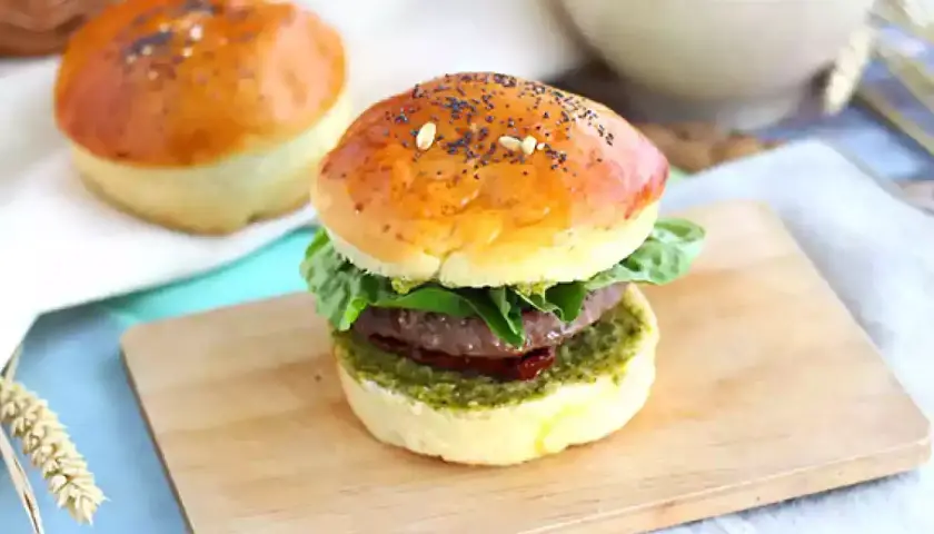 Pyszny burger włoski z soczystym mięsem, świeżą sałatą i aromatycznym pesto na złocistej bułce z makiem.