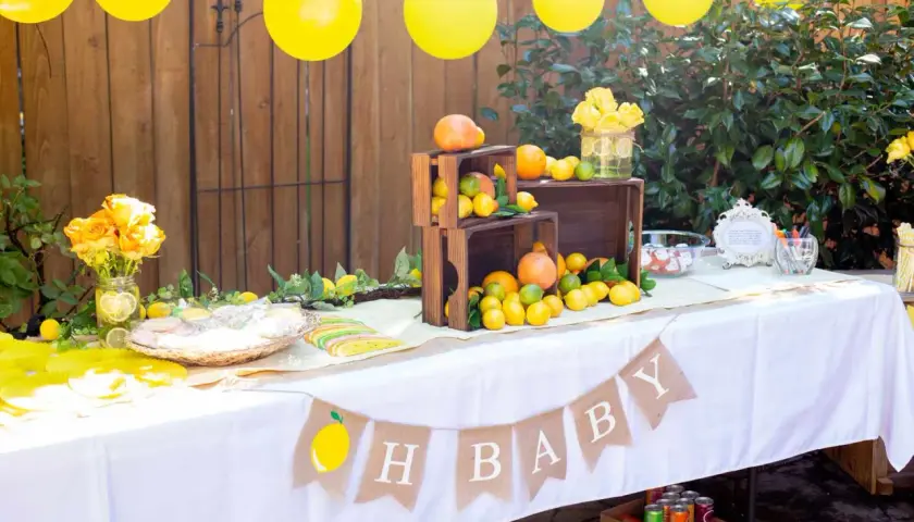 Udekorowany stół na baby shower z cytrynami, pomarańczami i żółtymi balonami.