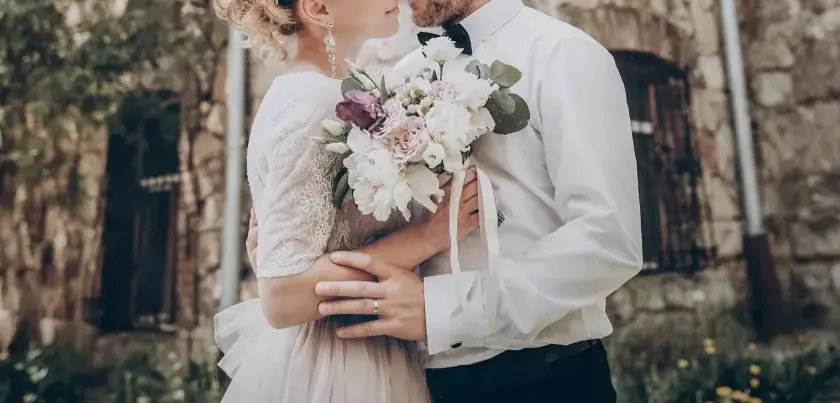 Para młoda trzyma bukiet kwiatów. Ich dłonie splecione na brzuchu panny młodej, na palcu obrączka. To piękny obrazek, jakby z kursu przedmałżeńskiego.