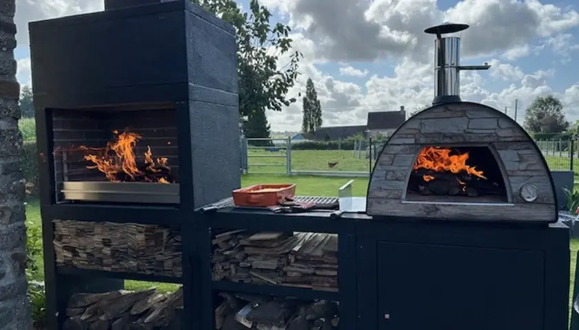 Un barbecue et un four à pizza en pierre, tous deux allumés, prêts pour un repas. Idéal pour savoir comment faire un barbecue sans charbon, avec du bois stocké en dessous.