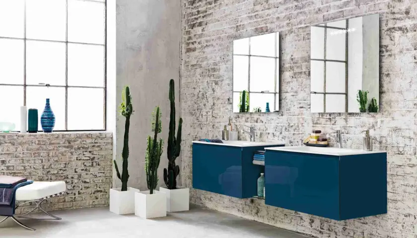Bagno moderno con mattoni a vista, piante di cactus e mobili sospesi blu. Diversi tipi di piastrelle per un look industriale.