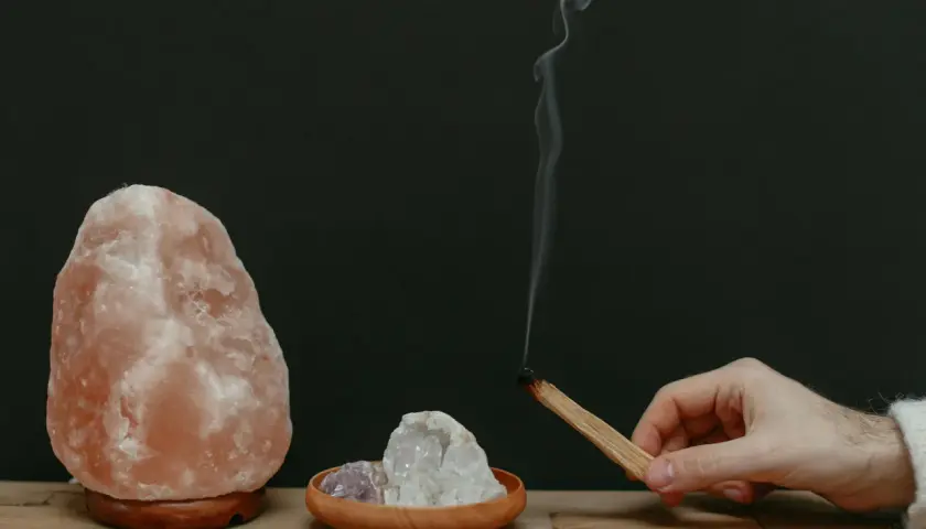Lámpara de sal rosa, cristales y un palo de incienso humeante.