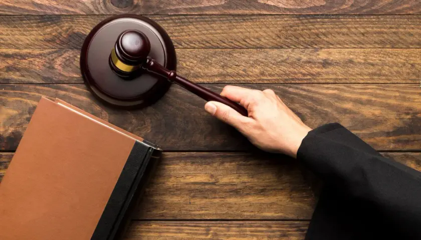 Młotek sędziowski i księga na drewnianym stole. Dłoń w czarnej todze przygotowuje się do uderzenia, symbolizując podział majątku i spółdzielcze lokatorskie prawo do lokalu.