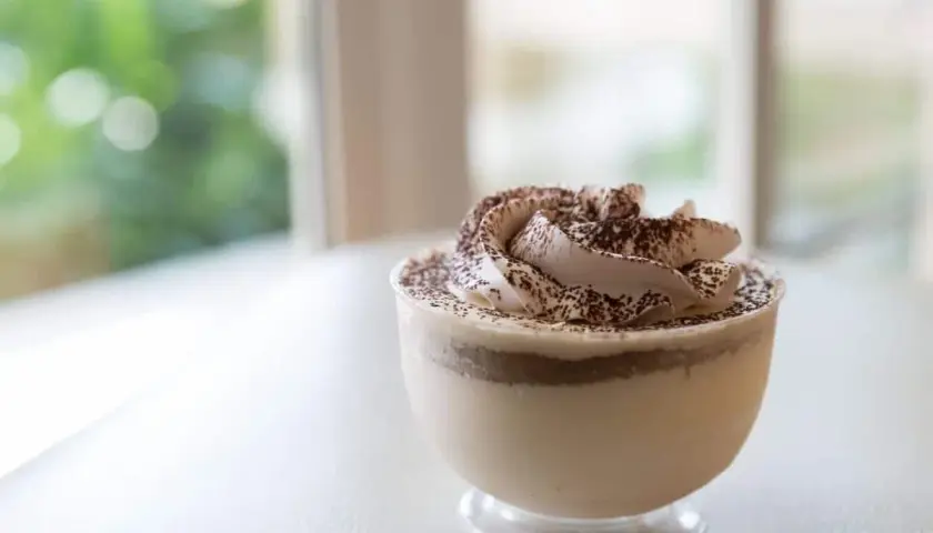 Delicioso mousse de café con crema batida y cacao espolvoreado, servido en un vaso transparente.