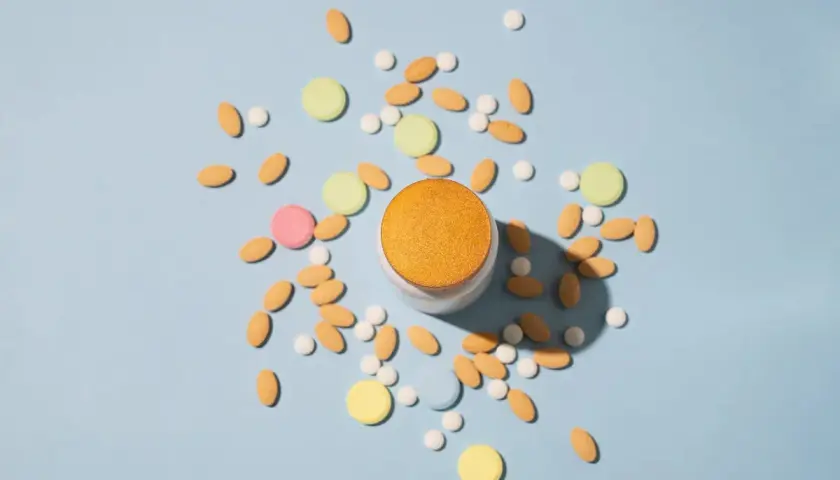 Pilules contraceptives et autres comprimés colorés dispersés autour d'un pot. Une solution pour l'acné ?