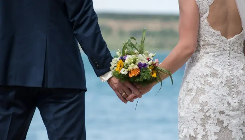 Para młoda trzyma się za ręce, trzymając bukiet kwiatów. Ceremonia ślubna w plenerze.