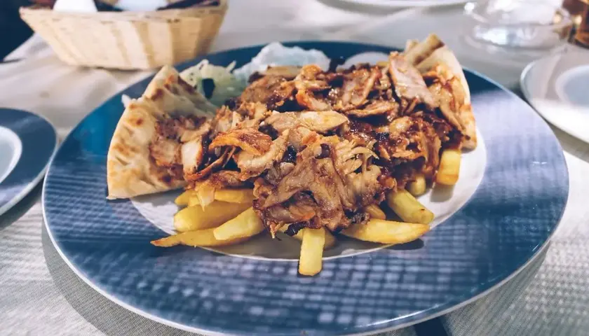 Pyszna szarma z kurczaka z frytkami i pitą na talerzu.