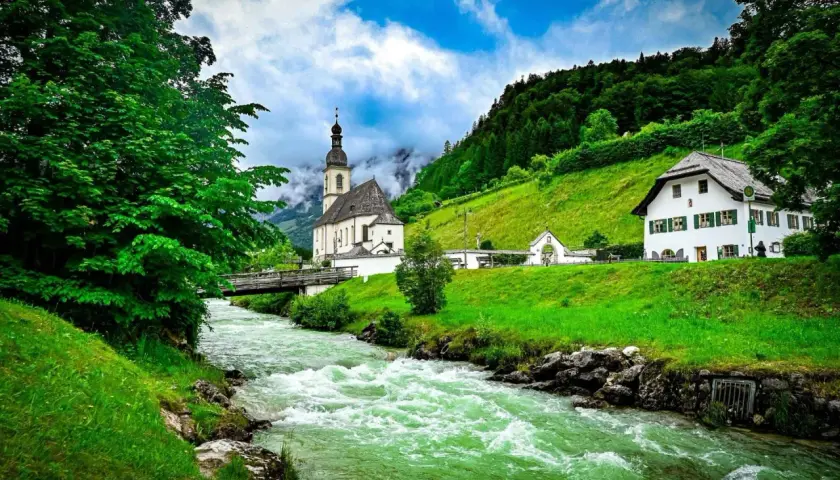 Grüner Fluss fließt an Kirche und Haus vorbei. Hier kann man in Berchtesgaden die Natur genießen und die Seele baumeln lassen.