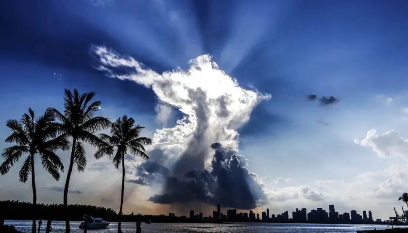 Dramatische Wolkenformationen im Himmel, die an eine engelhafte Gestalt erinnern, über einer Stadtkulisse mit Palmen. Ein Zeichen des Christentums?