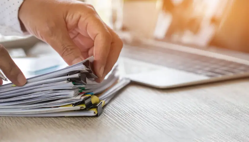 Dłoń przegląda stos dokumentów, szukając informacji, jak uzyskać odpis aktu urodzenia.
