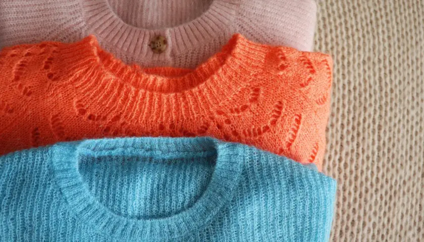 Gestapelte Pullover in Rosa, Orange und Blau. Der Wollprogramm-Waschmaschinen-Zyklus ist ideal für diese feinen Strickwaren.