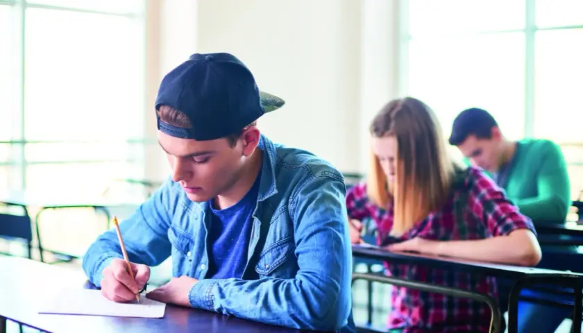 Ragazzo con cappellino scrive concentrato durante un esame. Il suo **did inglese** è importante per il futuro.