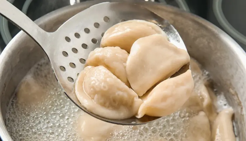 Gorące pierogi z serem, gotowane według przepisu babci, wyjmowane łyżką cedzakową z bulgoczącego garnka.