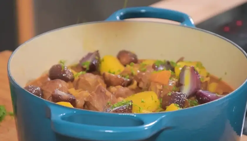 Un plat mijoté de navarin d'agneau, avec des morceaux de viande tendres, des carottes, des oignons rouges et des pommes de terre, garni de persil frais.