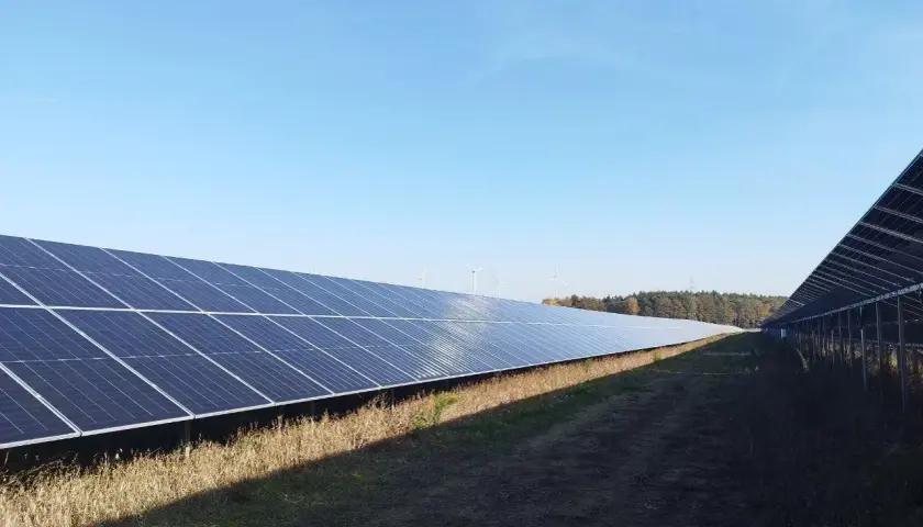 Panele słoneczne i wiatraki na tle błękitnego nieba. Dzierżawa ziemi pod farmę fotowoltaiczną to inwestycja, która może przynieść dochód.