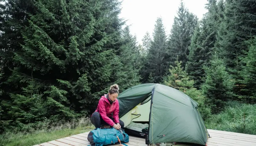 Une femme prépare son sac à dos près d'une tente dans une forêt de sapins. Une scène de camping en Allemagne.