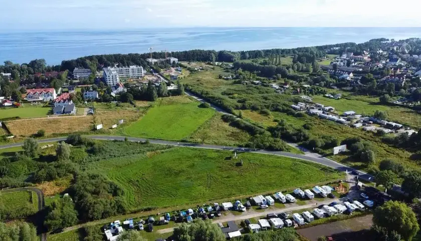 Widok z lotu ptaka na pole kempingowe w Kołobrzegu. Widać morze, zabudowania i wiele kamperów oraz przyczep kempingowych.