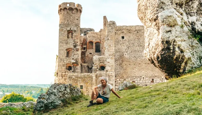 Kobieta odpoczywa na trawie przy ruinach zamku, idealne miejsce na przerwę podczas podróży szlakiem Orlich Gniazd samochodem.