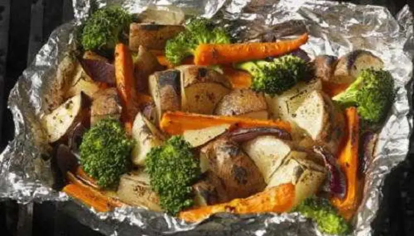 Légumes variés (pommes de terre, carottes, brocolis, oignons rouges) cuits en papillote sur un barbecue, prêts à être dégustés.