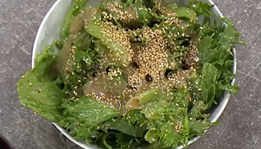 Grön, krispig sallad med sesamfrön och en dressing, perfekt som sallad till paj.