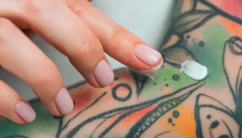 Main d'une personne appliquant une crème sur un tatouage coloré. Si vous suspectez une infection tatouage, que faire ? Consulter un professionnel de santé.