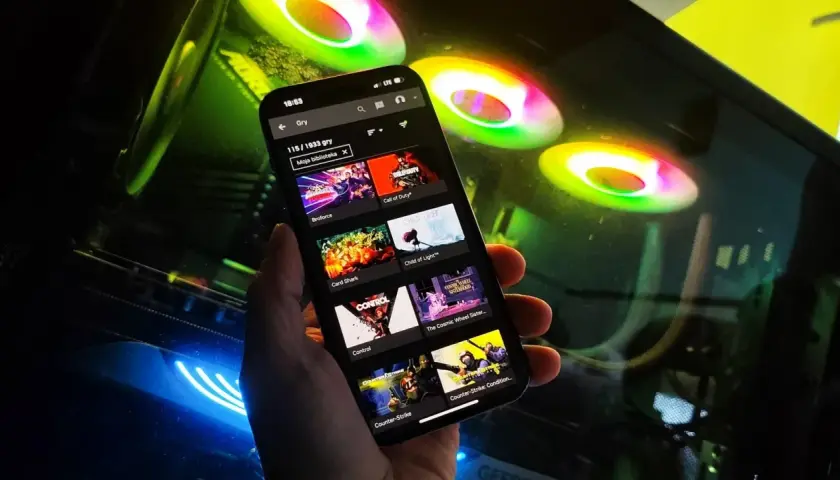Przeglądanie listy gier na GeForce Now na telefonie, w tle świecące wentylatory komputera.