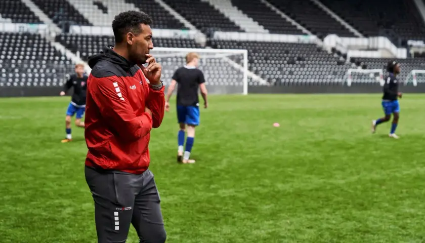 Ein Mann in Rot und Schwarz beobachtet aufmerksam junge Fußballer auf dem Trainingsplatz. Ein typischer Tag im Leben eines Fußball Scout.