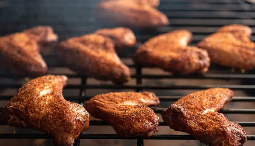 Ailes de poulet marinées pour barbecue, grillées à la perfection, dégageant une fumée alléchante.