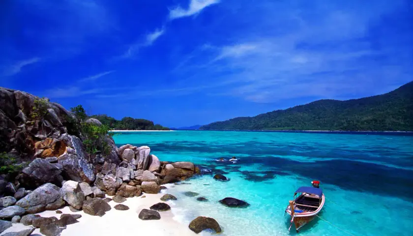 Traumhafte Bucht mit Felsen, weißem Sand und türkisfarbenem Wasser. Ein Boot liegt vor Anker. Perfekt für die beste Reisezeit Thailand.