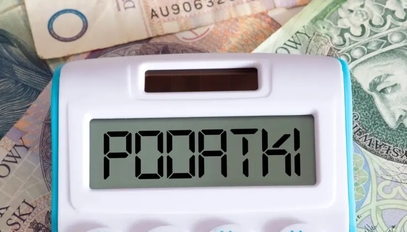 Kalkulator z napisem "PODATKI" na tle polskich banknotów. Czas na rozliczenie PIT 28 druk.