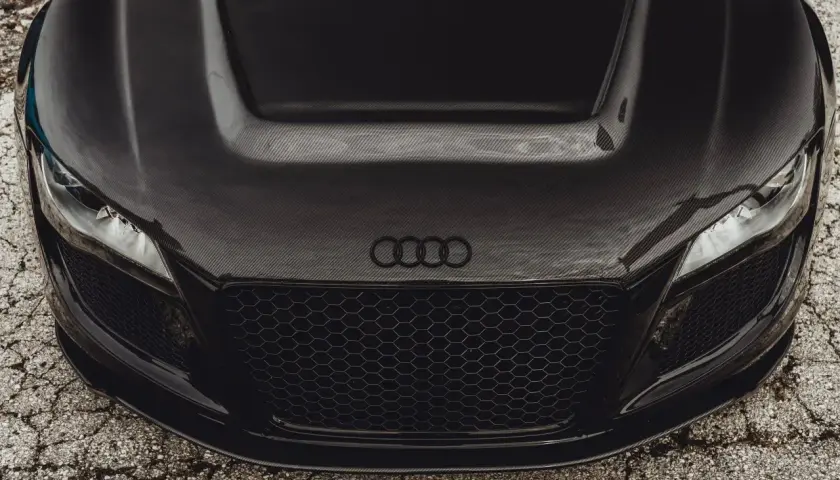 Przód czarnego auta sportowego z maską z włókna węglowego. Widać reflektory, grill i logo Audi.