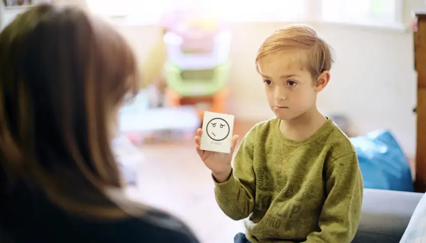 Chłopiec trzyma kartkę z rysunkiem smutnej buźki i napisem "SORRY".