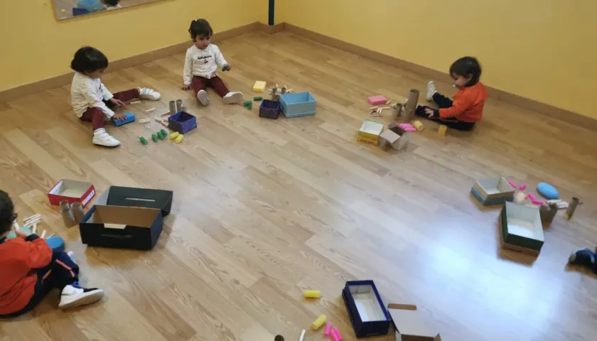 Niños pequeños exploran materiales diversos, cajas y pinzas, aprendiendo sobre el juego heurístico.