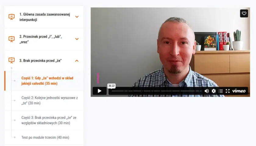 Mężczyzna w kratę tłumaczy, kiedy nie stawiamy przecinka przed "że", omawiając jego użycie w składzie całostki.