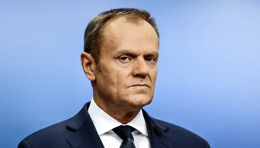 Portret Donalda Tuska w granatowym garniturze i białej koszuli na jasnoniebieskim tle.