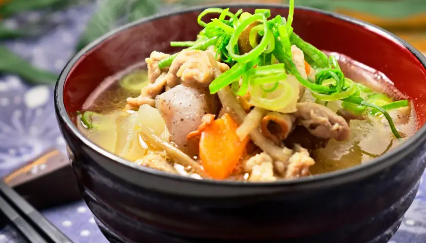 A steaming bowl of tonjiru recipe, filled with pork, vegetables, and topped with fresh green onions.