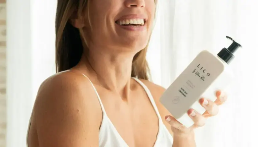 Mujer sonriente sostiene un acondicionador LICO. Descubre para qué sirve el acondicionador del pelo: suavidad y brillo.
