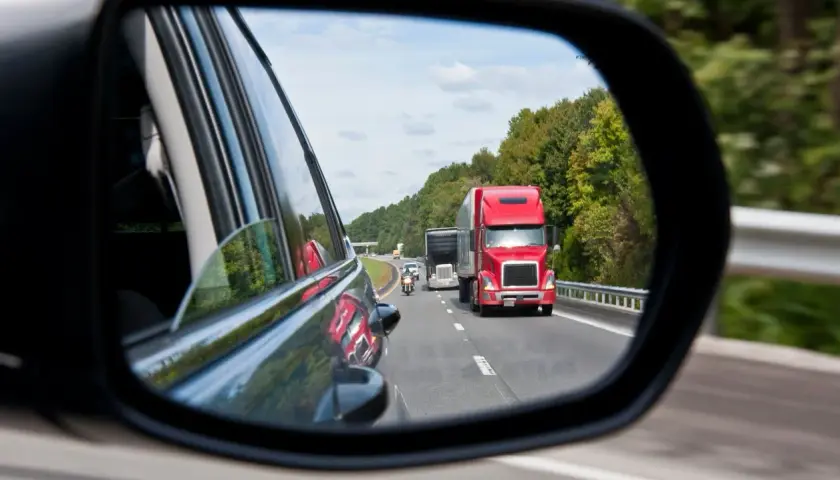 Reflejo en el espejo retrovisor: un camión rojo y una moto circulan por la carretera. ¡Atención! una moto puede adelantar por la derecha.