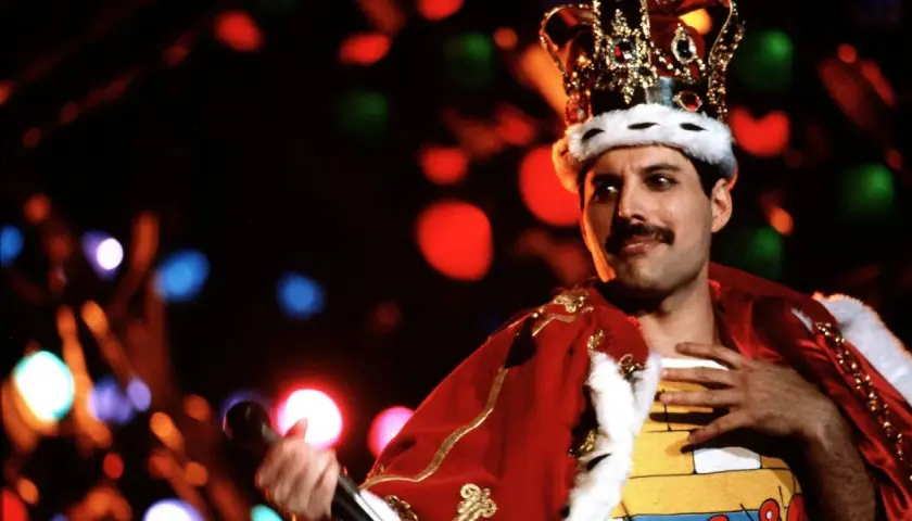 Freddie Mercury w koronie i czerwonym płaszczu, śpiewający swoje legendarne piosenki.
