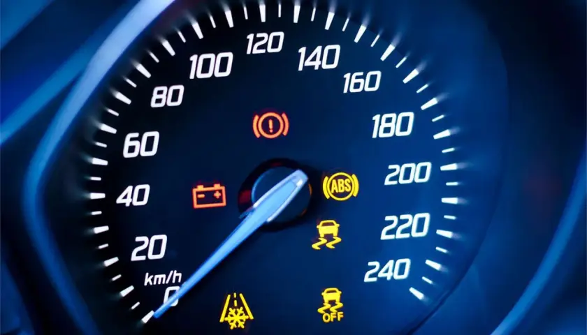 Cruscotto auto con tachimetro e spie accese: spia punto esclamativo giallo, ABS, controllo stabilità e batteria.