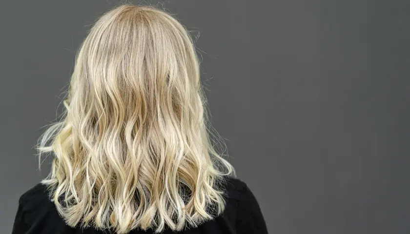 Widok z tyłu na falowane, blond włosy kobiety na ciemnym tle.