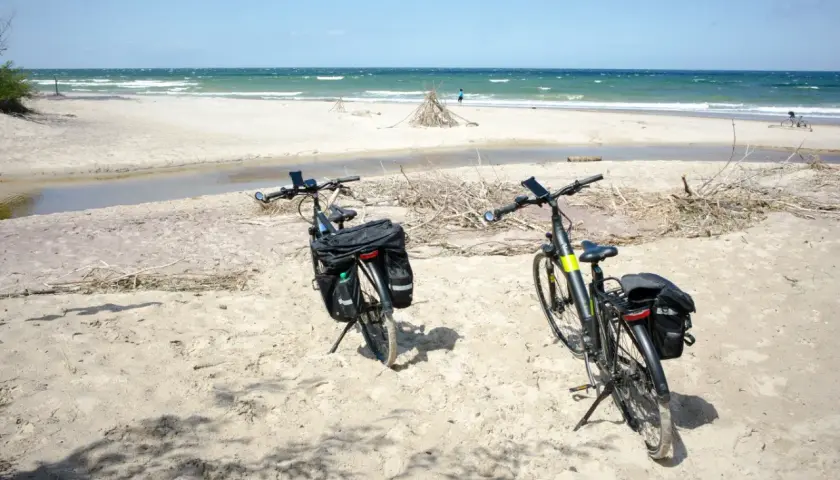 Dwa rowery z sakwami na piaszczystej plaży, gotowe na odkrywanie tras rowerowych nad morzem.